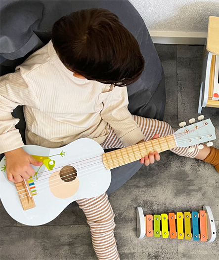 Niño tocando la guitarra acústica de madera de iniciación musical Montessori